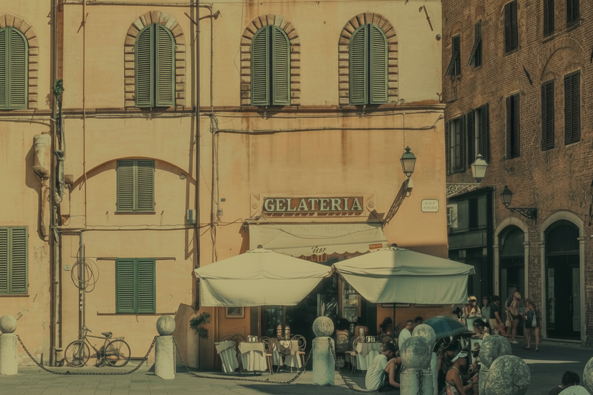 A scenic photograph of a European town square with warm-toned buildings, shuttered windows, outdoor cafe umbrellas, and stone bollards in the foreground.
